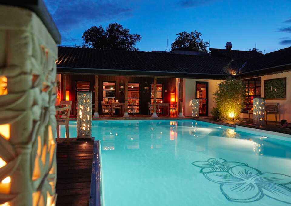 Beleuchteter Swimmingpool am Abend mit Frangipani-Muster auf dem Beckenboden
