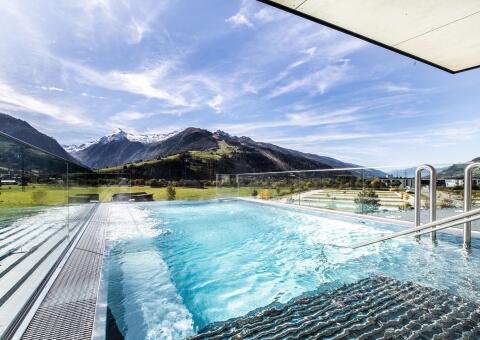 Moderner Außenpool mit Glasbrüstung und Panoramablick auf ein schneebedecktes Bergmassiv.