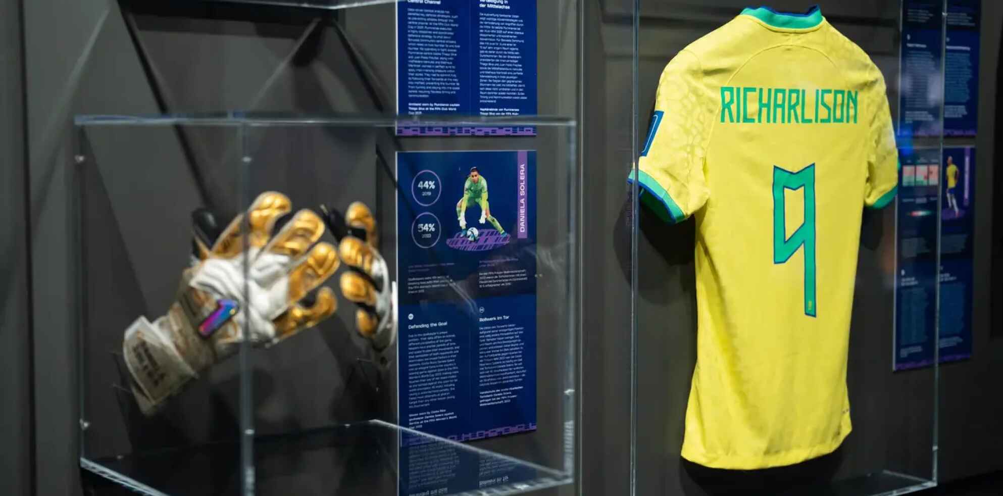 Ausstellungsvitrinen in einem Fußballmuseum mit gold-weißen Torwart-Handschuhen in einem Glaskasten und dem gelben brasilianischen Trikot von Richarlison mit der Nummer 9. RICHARLISON 9.